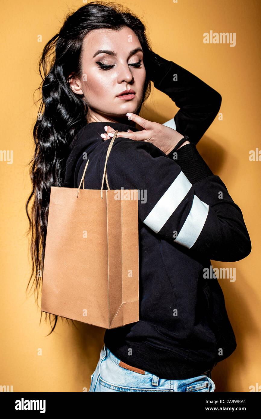 Happy brunette Mädchen hält einen Kauf in ein Handwerk Tasche auf orangem Hintergrund. Stockfoto