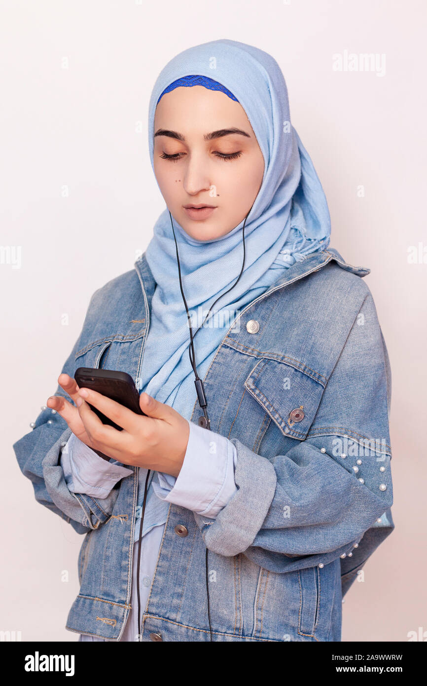 Moderne muslimische Mädchen hört Musik, Podcasts und Hörbücher auf dem Smartphone. Happy muslimischen Frau im hijab Anhören von Demo-Songs mit Kopfhörer. Schöne Mitte Stockfoto