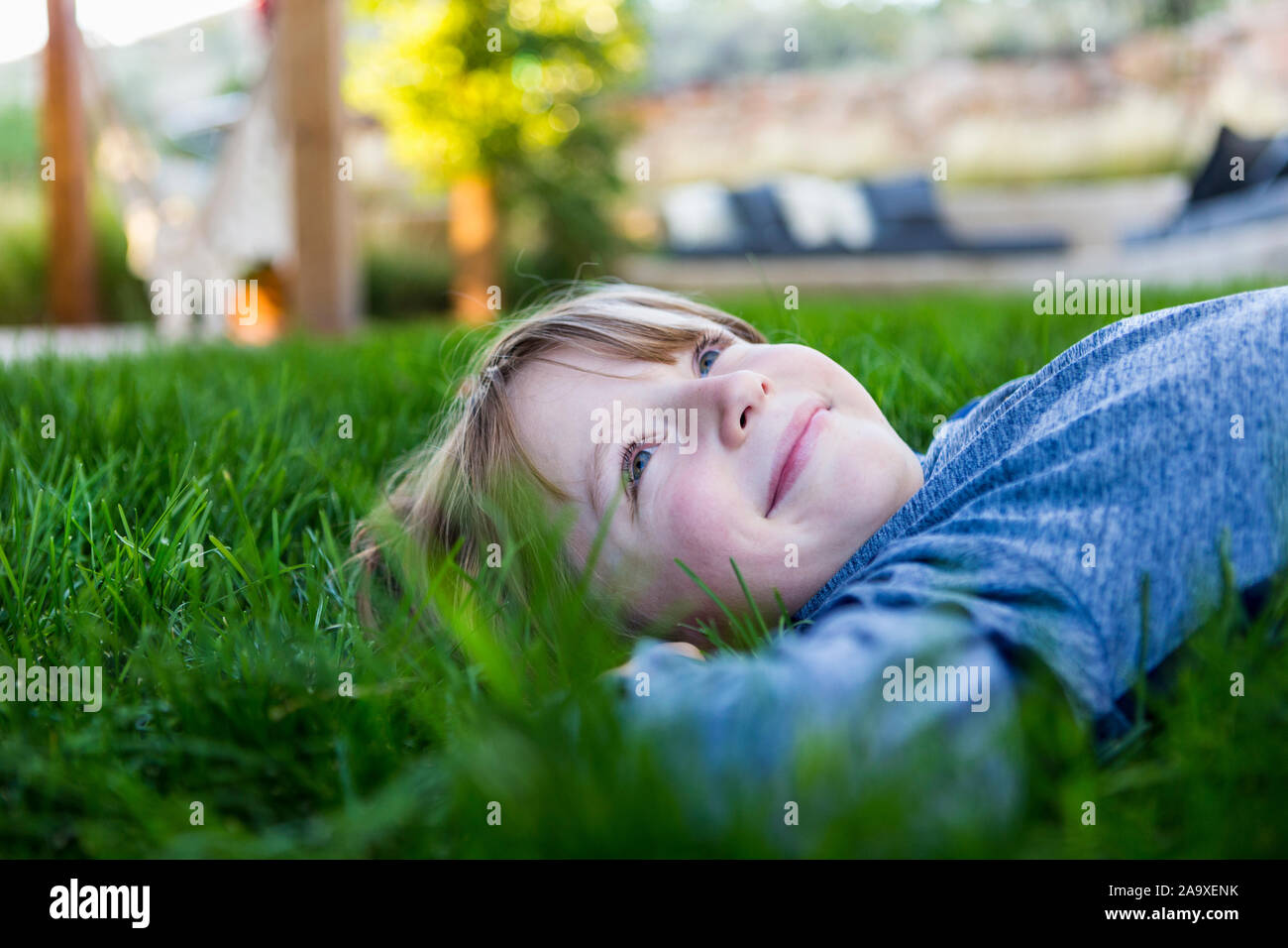 Portrait von LÄCHELNDEN 6-jährigen Jungen, der sich im grünen Gras Stockfoto