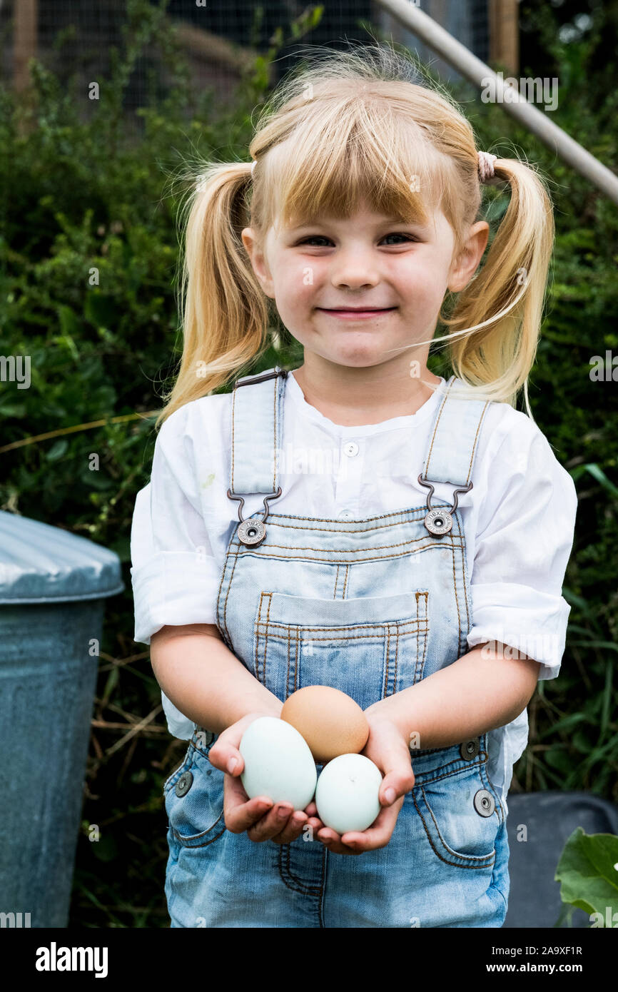 Blonde Mädchen stehen in einem Garten, frische Eier, lächeln in die Kamera. Stockfoto