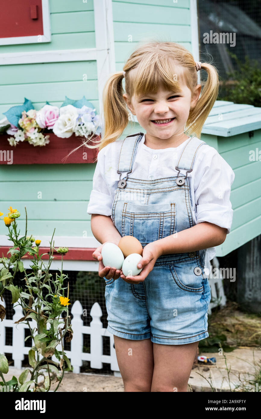 Blonde Mädchen stehen in einem Garten vor der henne haus, halten frische Eier. Stockfoto