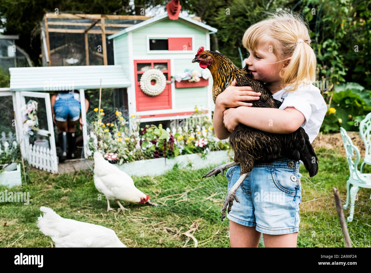 Blonde Mädchen stehen in einem Garten vor der henne haus, braun Huhn. Stockfoto