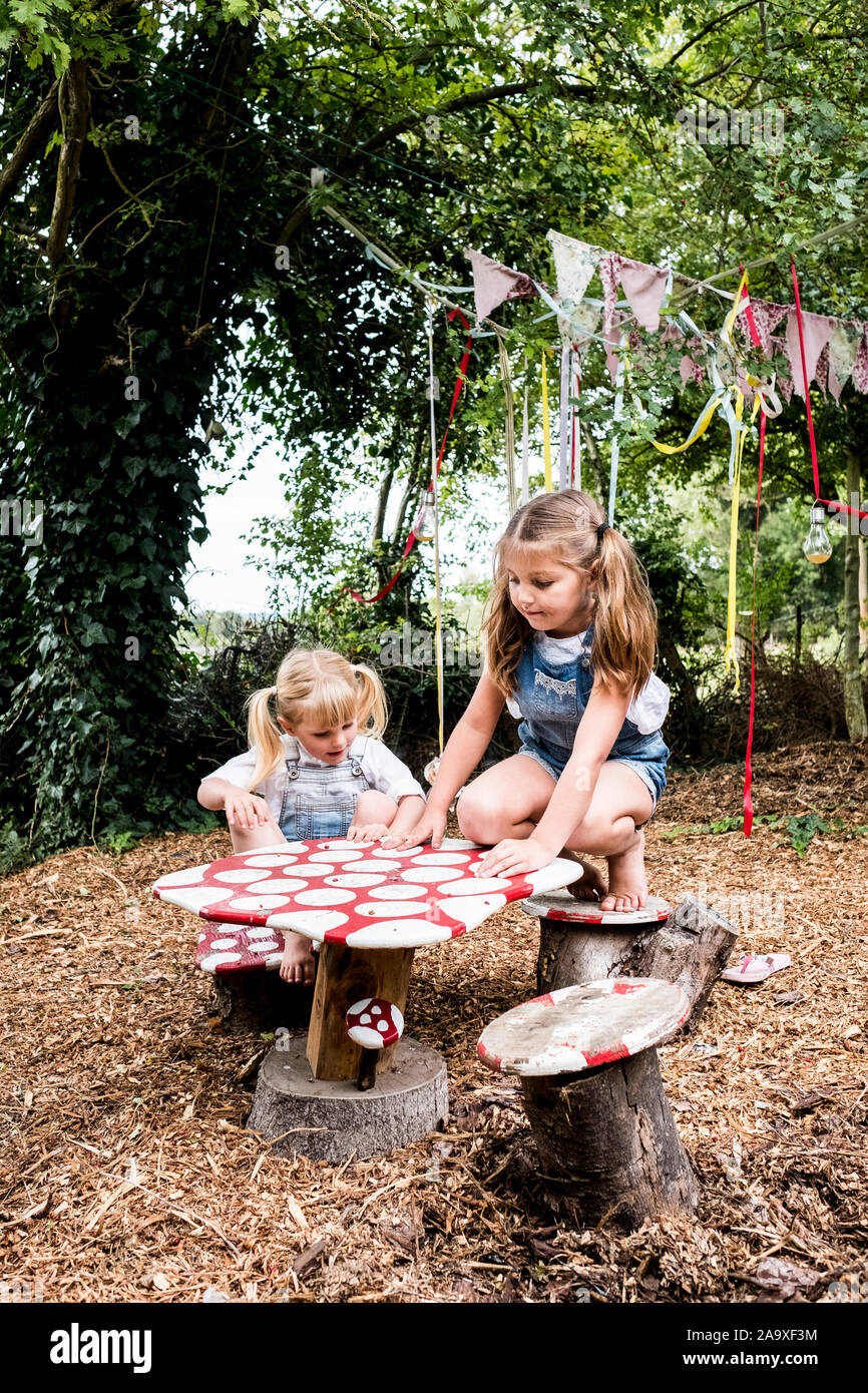 Zwei Mädchen sitzen an kleinen Holztisch im Garten spielen. Stockfoto
