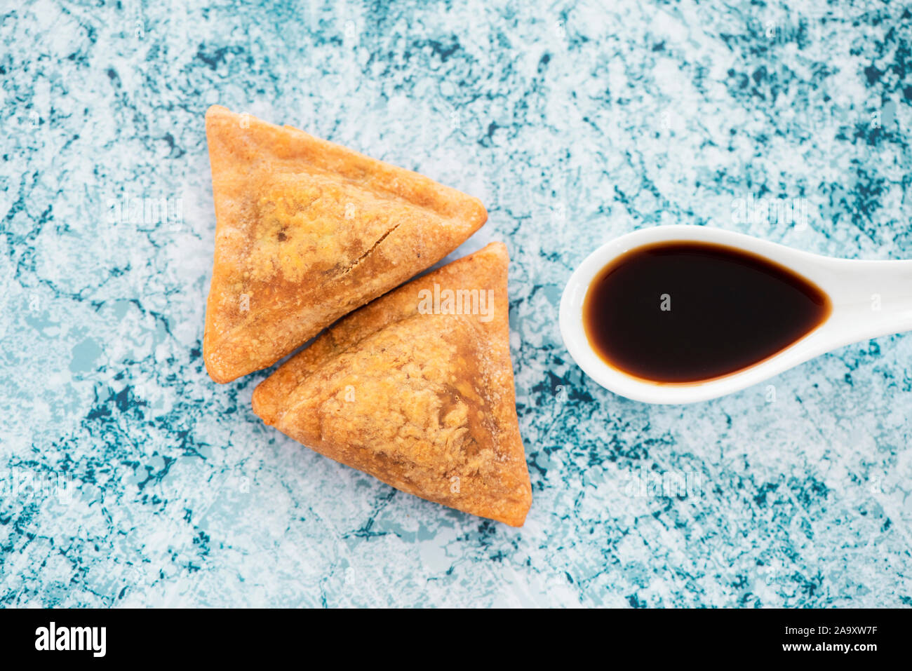 Hohen winkel Blick auf einige indische Samosas und einem keramischen Löffel mit einem dunklen Soße auf einer Marmor Stein Oberfläche Stockfoto