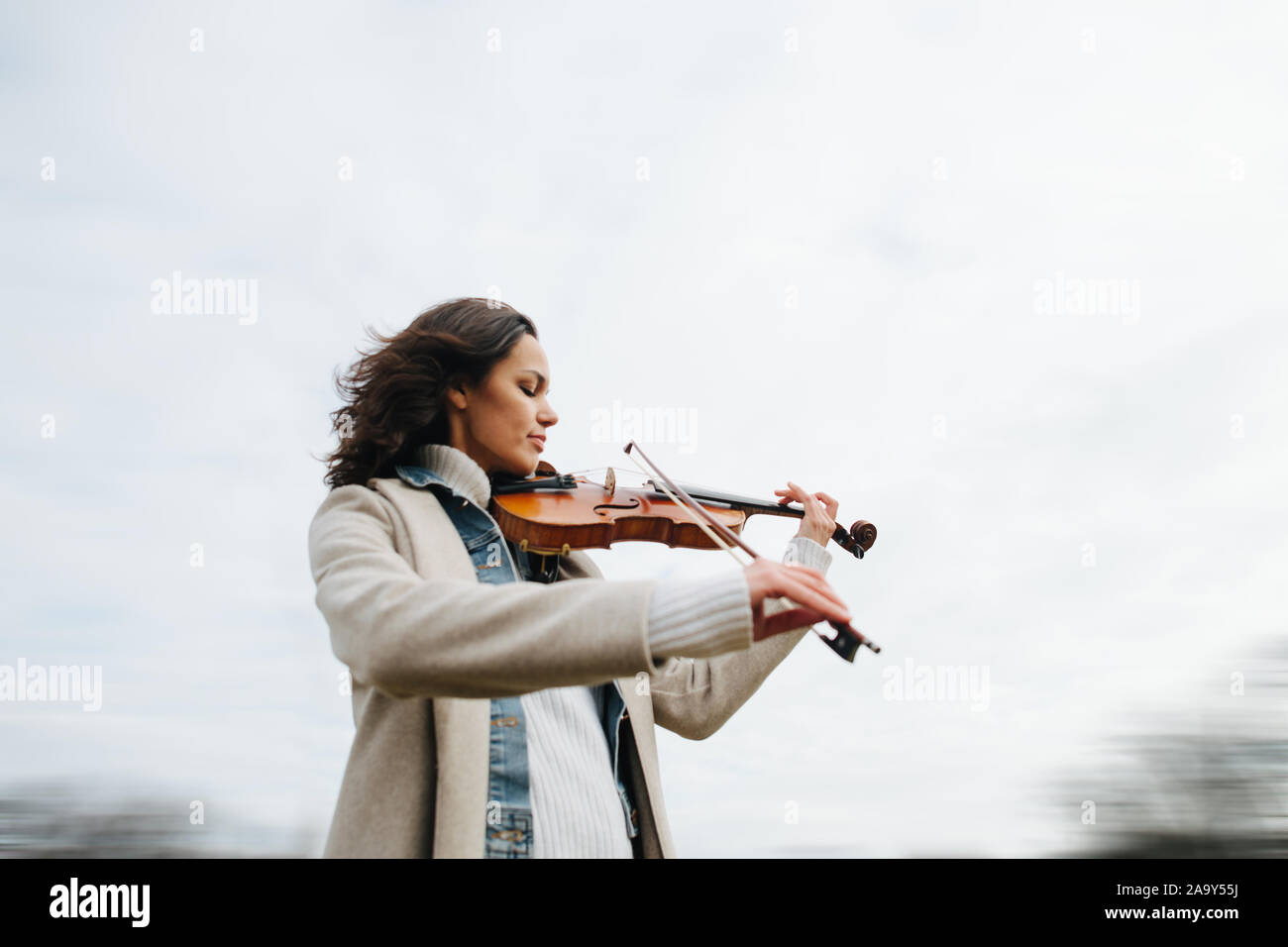 Schöne Frau in einen Mantel spielt Violine im Freien mit geschlossenen Augen Stockfoto