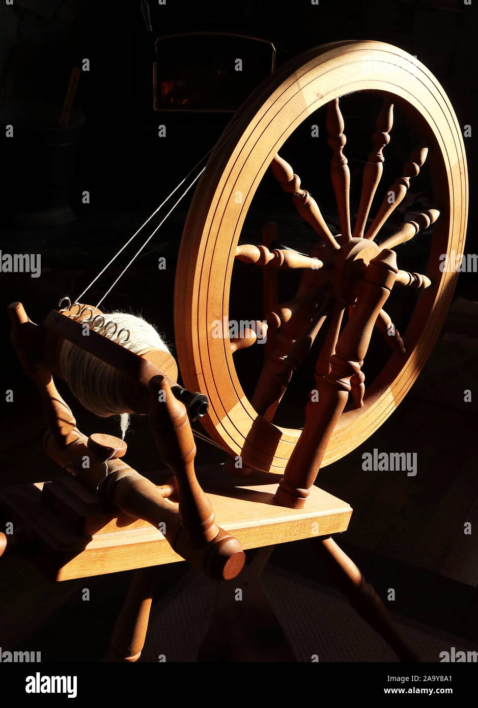 Sachsen style Double Drive Spinning Wheel in einem sonnigen Patch mit dem dunklen Raum und Feuer hinter. Stockfoto