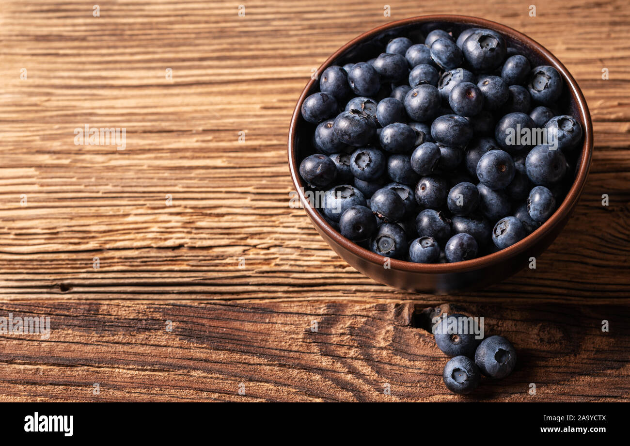 Frische reife Heidelbeeren in braun Keramik Schüssel auf Holz- Hintergrund, Zutaten für gesunde Ernährung lifestyle Konzept, 45 Grad Winkel betrachten, horizontal Stockfoto