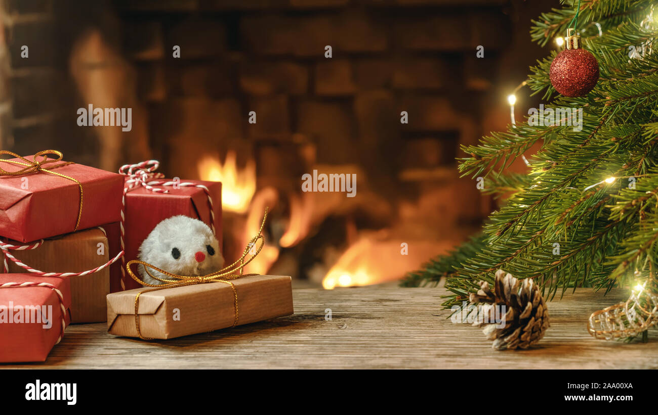 Weihnachten Komposition - Maus ist Symbol des 2020 nach dem chinesischen Horoskop neben Geschenke unter dem Weihnachtsbaum im Zimmer mit Kamin. Stockfoto
