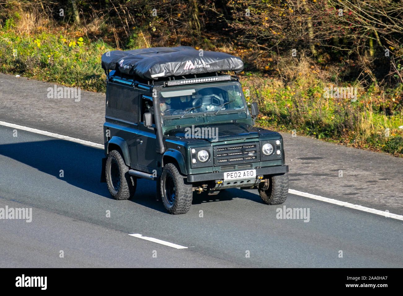 2002 grüner Land Rover Defender 90 County TD5; mit Schnorchelauspuff, Fahrzeugverkehr in Großbritannien, Transport, moderne Fahrzeuge, Salonwagen, südwärts fahrendes Fahren auf der 3-spurigen Autobahn M6. Stockfoto