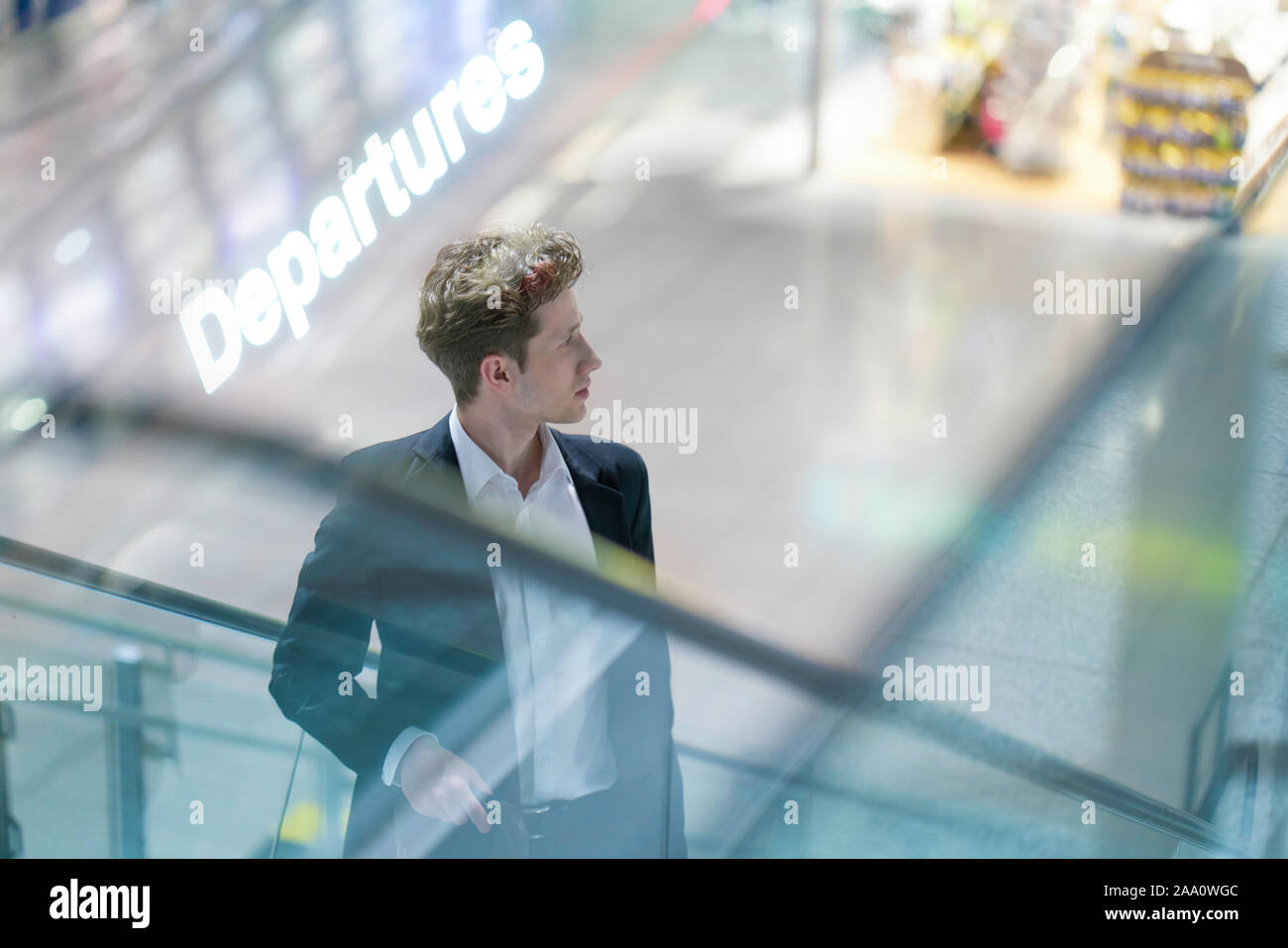 Junge Geschäftsmann im Anzug auf einer Rolltreppe am Flughafen mit seinem Gepäck, unscharfen Hintergrund, double explosure mit Abfahrten Stockfoto