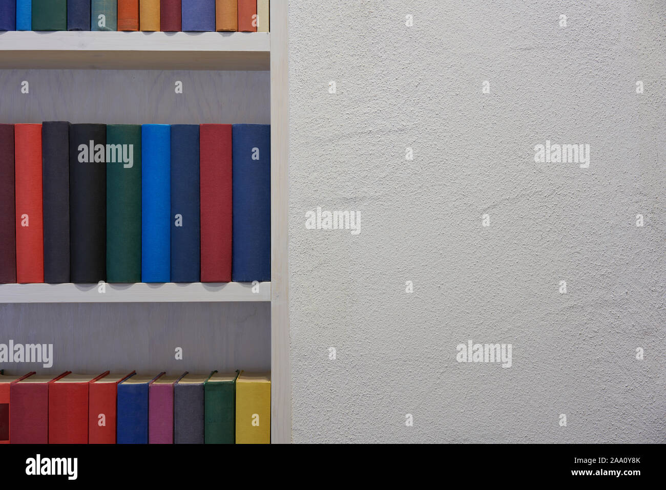 Weiß verputzte Wand mit bunten Bücher im Regal Stockfoto