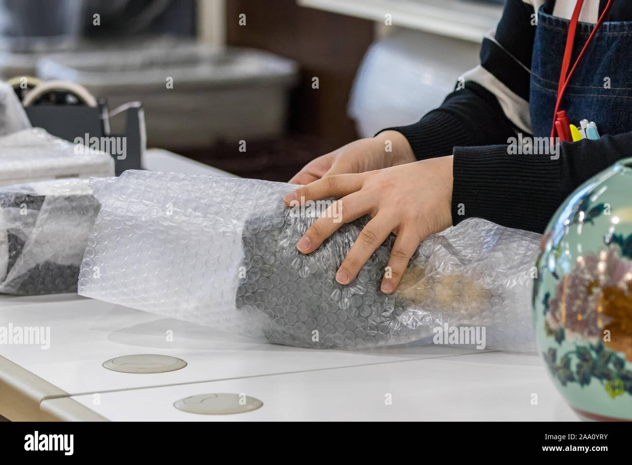 Weibliche Verkäufer Hände wickeln ein Produkt mit Luftpolsterfolie Schutzmaßnahmen an der Ladentheke, innen Stockfoto