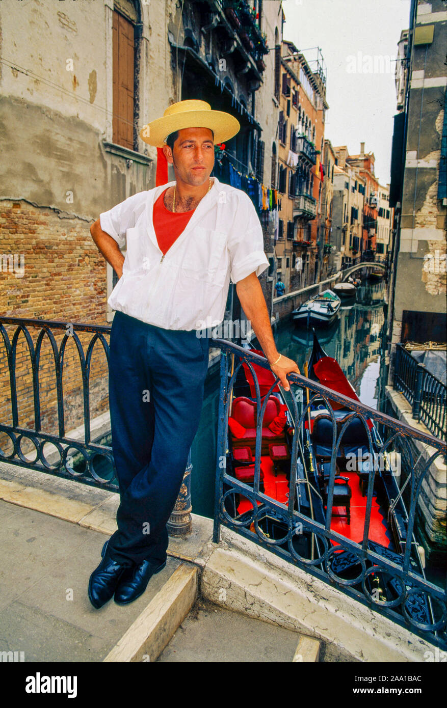 Das Tragen der traditionellen Kleidung und Hut, ein gondoliere wartet auf Passagiere auf einem Kanal in Venedig, Italien, mit seiner Gondel im Hintergrund. MODEL RELEASE Stockfoto