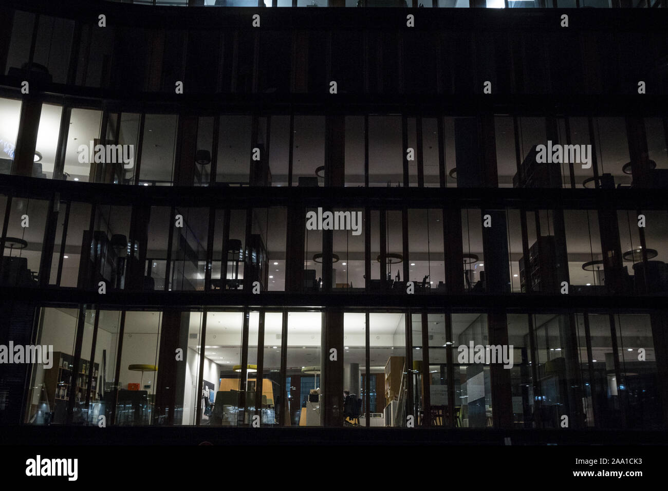 Fassade eines Geschäftsviertels Gebäude, ein Hochhaus, in der Nacht, abends, mit nur ein paar Fenster beleuchtet, und ein Mitarbeiter allein in diesem späten Arbeiten Stockfoto