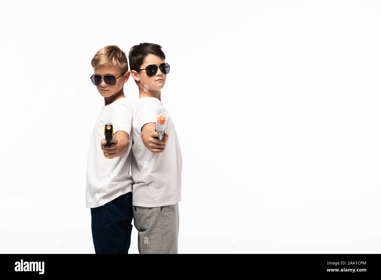 Zwei Brüder in Sonnenbrille Rücken an Rücken und darauf abzielen, mit Spielzeugpistolen an Kamera beim Spielen Gangster isoliert auf weißem Stockfoto