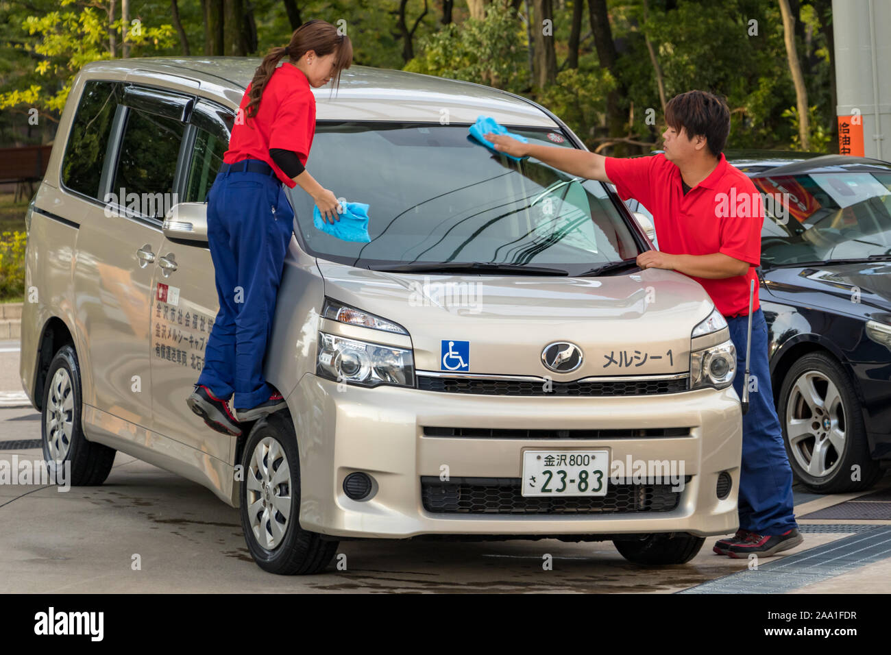 Zwei weibliche und männliche Japanische Tankstelle Arbeiter, die Reinigung der Windschutzscheibe eines Kunden Auto in Kanazawa, Japan. Stockfoto