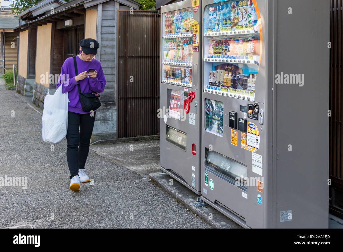 Eine junge Japanerin texting - Chatten mit Ihren mobilen Neben einem automatischen Getränke Anbieter Maschine in Kanazawa, Japan. Stockfoto