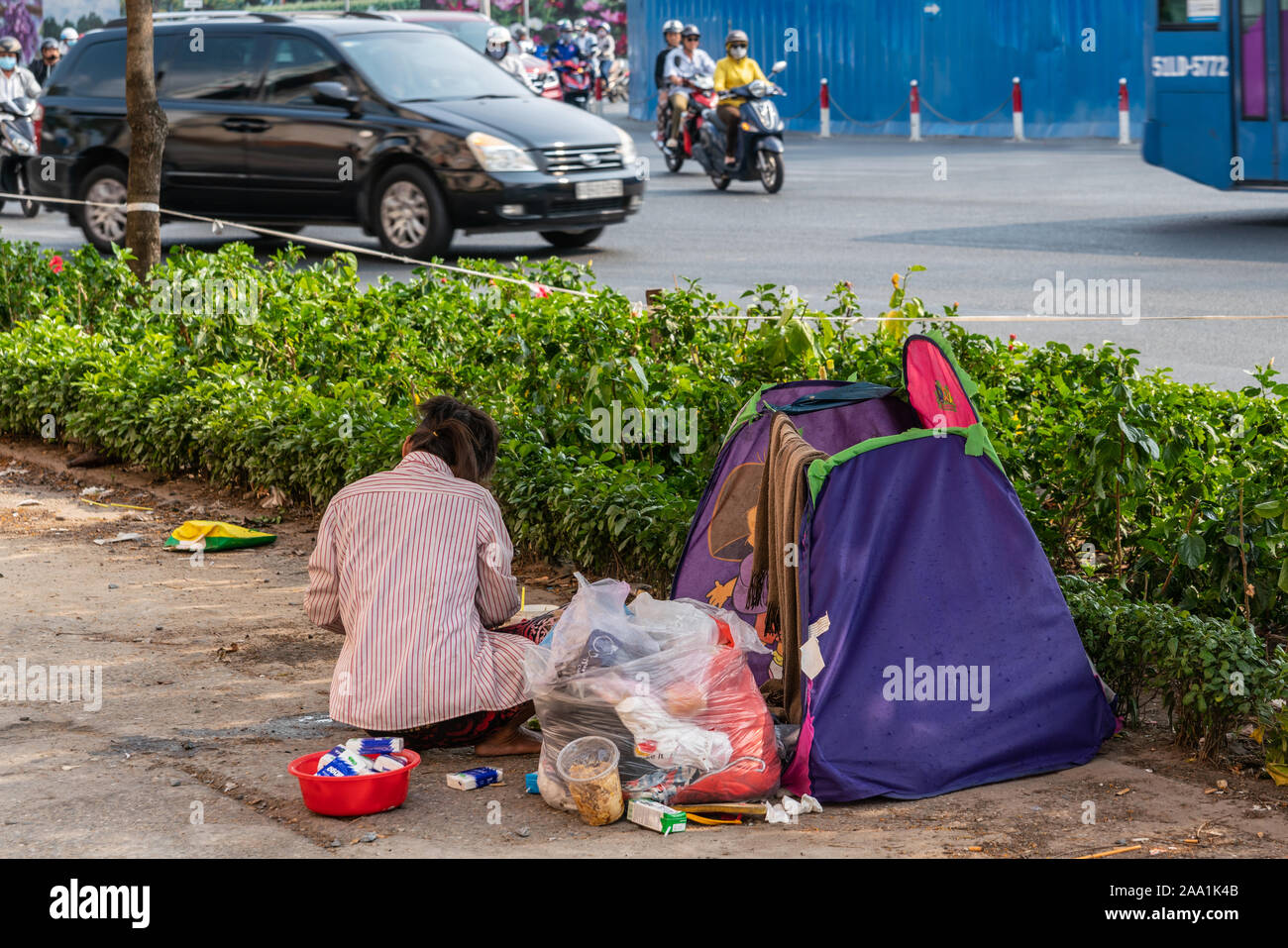 Ho Chi Minh City, Vietnam - 12. März 2019: Straße der Innenstadt Landschaft. Obdachlose Frau in rot gestreiften weißen Hemd mit Ihrem kleinen Zelt und Plastikbeutel wi Stockfoto