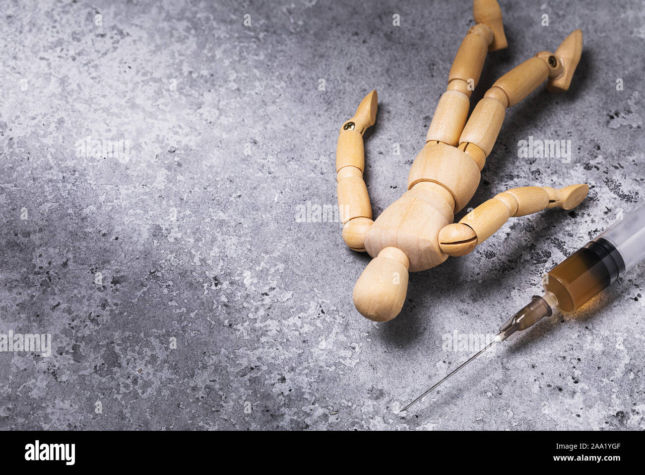 Eine Spritze mit Drogen und daneben liegt die Abbildung eines Mannes aus Holz. Süchtiger auf dem Boden. Konzept zum Thema Drogen Entzug mit Kopie spac Stockfoto