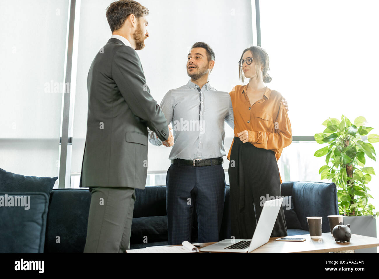 Junge und glückliche Paar in einem Abkommen, das Händeschütteln mit finanzieller Berater oder real estate agent Im luxuriösen Büro Stockfoto