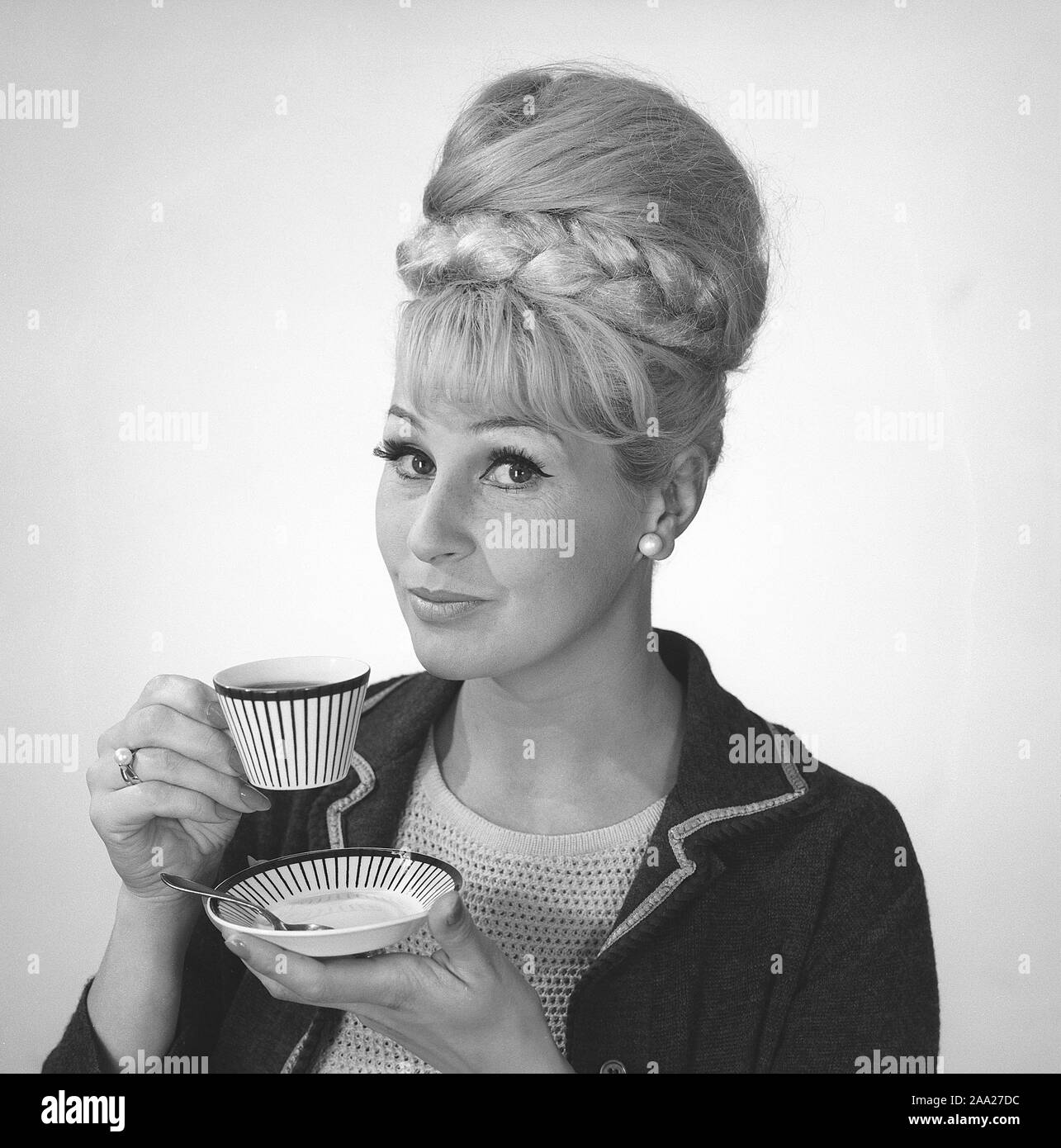 Kaffee in den 1960er Jahren. Eine Frau trinkt Kaffee aus einer Kaffeetasse mit einem 1960er Streifenmuster. Sie hat ihr Haar in den typischen Bienenstock Frisur, in denen lange Haare auf dem Kopf aufgetürmt ist und eine gewisse Ähnlichkeit mit der Form eines traditionellen Bienenstock. Schweden 1962. Ref BV 97-8 Stockfoto