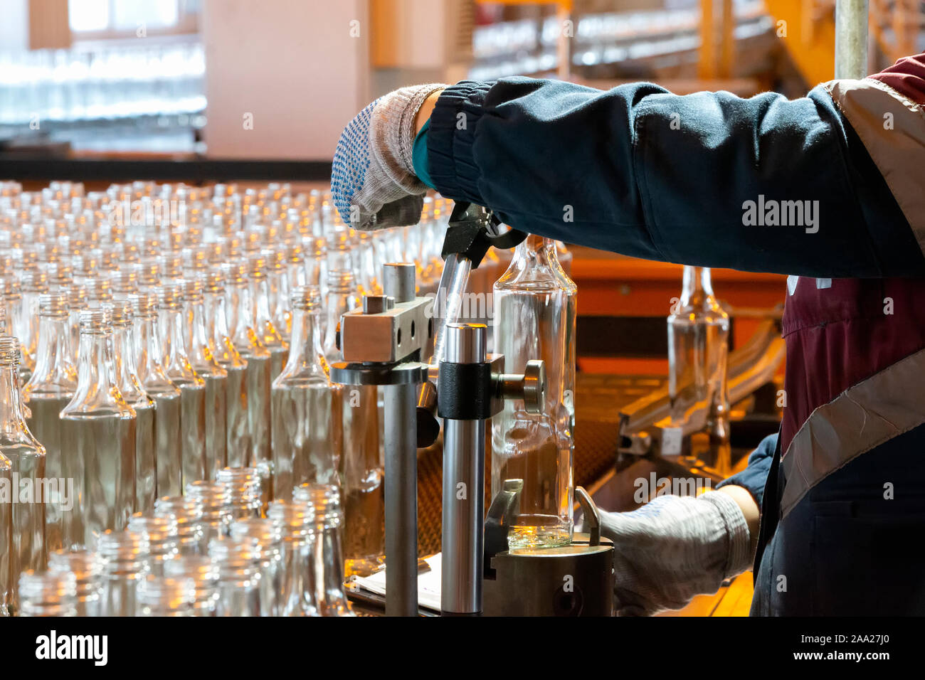 Glashütte. Glasindustrie. Die Hände halten eine Glasflasche auf dem Hintergrund eines Förderbandes. Stockfoto