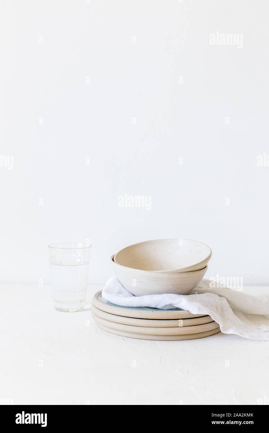Stapel von keramischen Platten und Schüsseln neben einem Glas Wasser Stockfoto