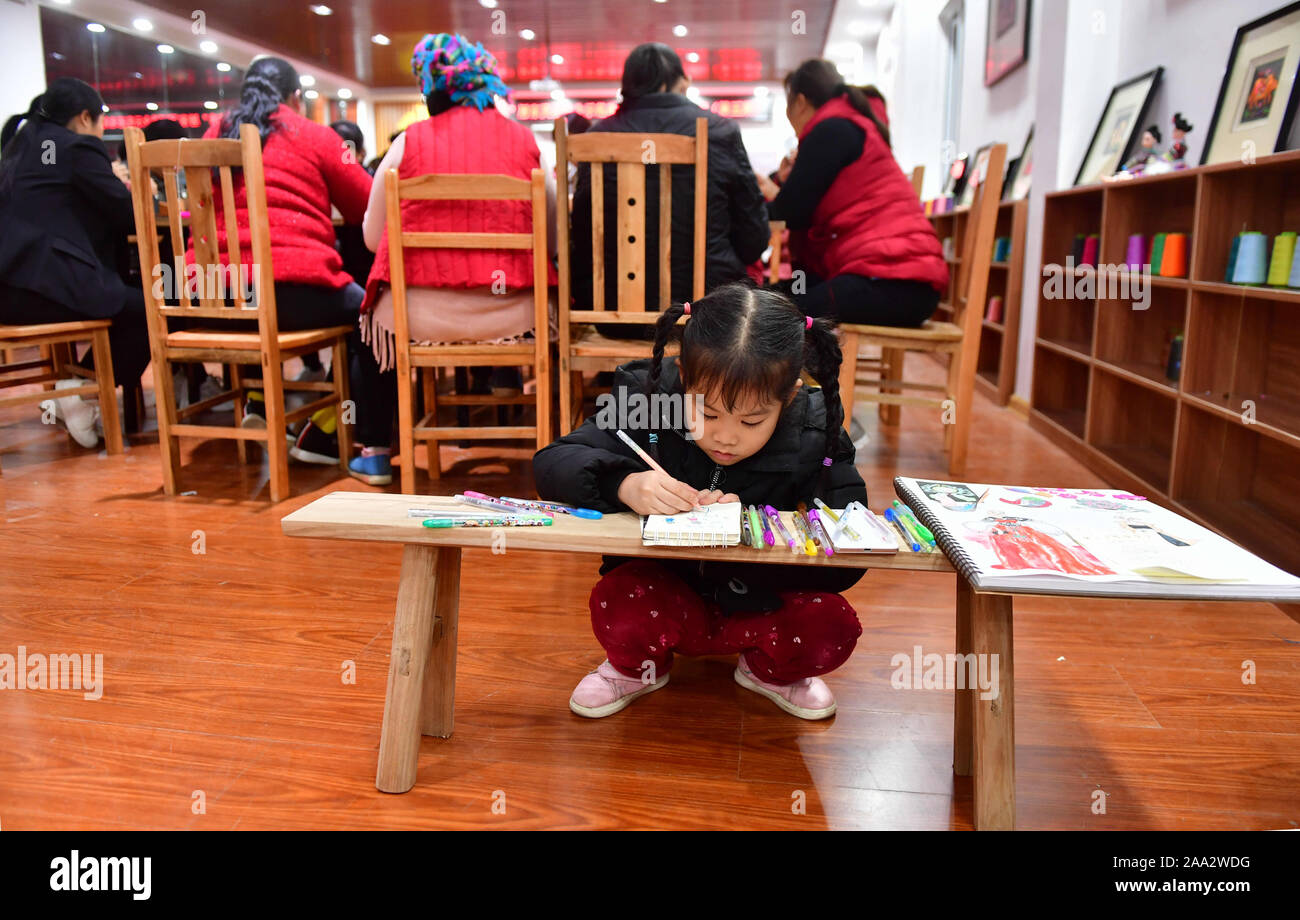 Rongshui, China Guangxi Zhuang autonomen Region. Nov, 2019 18. Die 5-jährige Mädchen Yang Dongning malt Bilder, während ihre Mutter nimmt eine Stickerei Klasse auf einem Workshop in Rongshui Miao autonomen County, South China Guangxi Zhuang autonomen Region, Nov. 18, 2019. Seit April dieses Jahres, eine Nacht Schule wurde von der lokalen Regierung der ländlichen Frauen in der Stickerei zu trainieren, damit deren Möglichkeit, der Armut zu verbessern. Bisher sind fünf halben Monat Kurse stattgefunden haben, mit fast 400 Frauen ausgebildet, um die Fähigkeiten zu meistern. Credit: Huang Xiaobang/Xinhua/Alamy leben Nachrichten Stockfoto