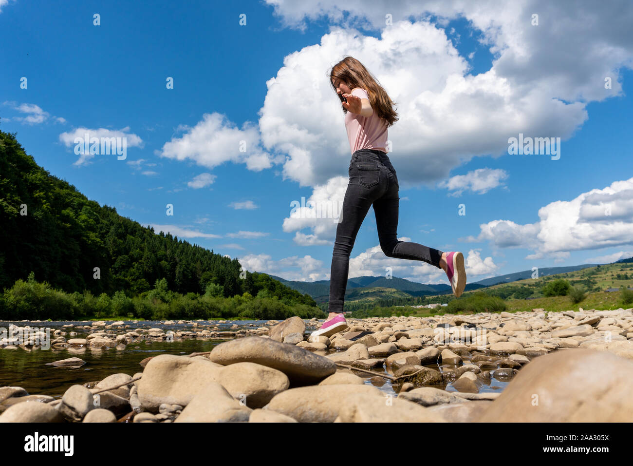 Junges Mädchen springen von Stein zu Stein auf mountain river Stockfoto