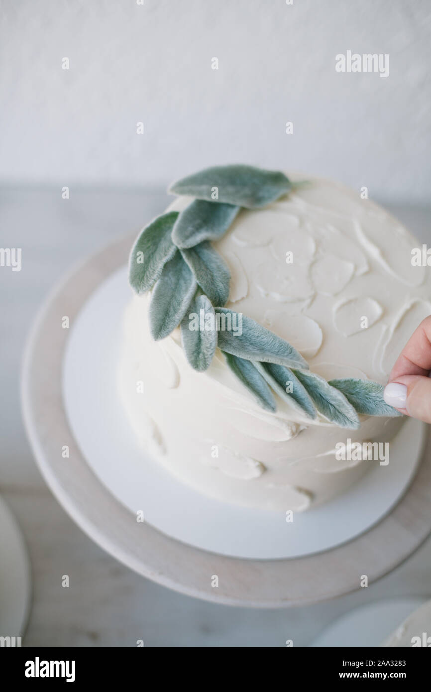 Frau Verzieren eines buttercream Vereisung Kuchen mit Blättern Stockfoto