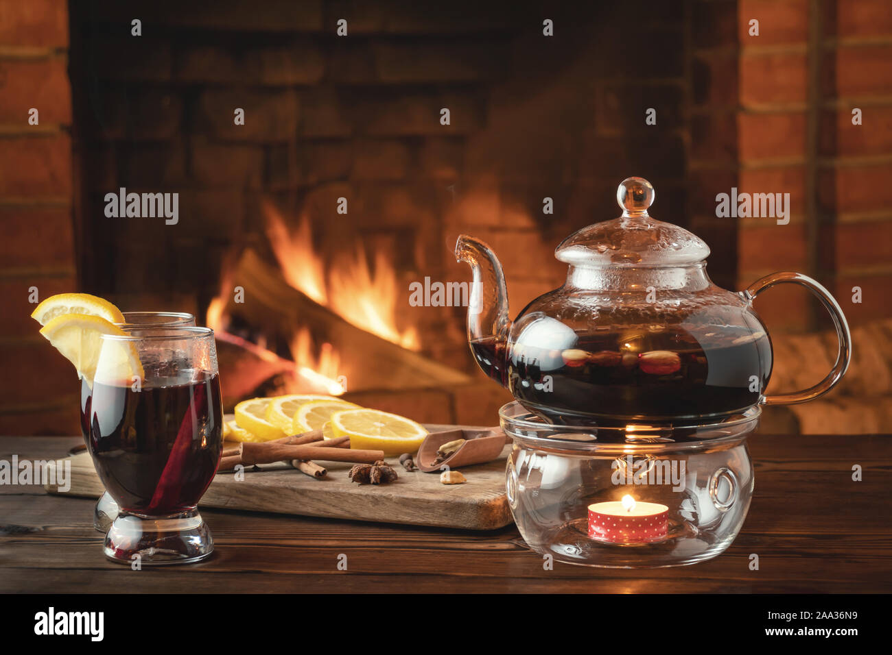 Zwei Gläser von Glühwein und Teekanne auf einem holztisch vor einem brennenden Kamin. Stockfoto