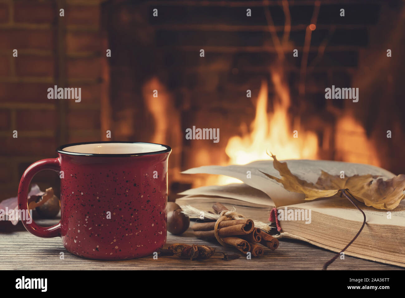 Rot Tasse mit heißem Tee und ein offenes Buch vor einem brennenden Kamin, Komfort, Entspannung und Wärme des Herdes Konzept. Stockfoto