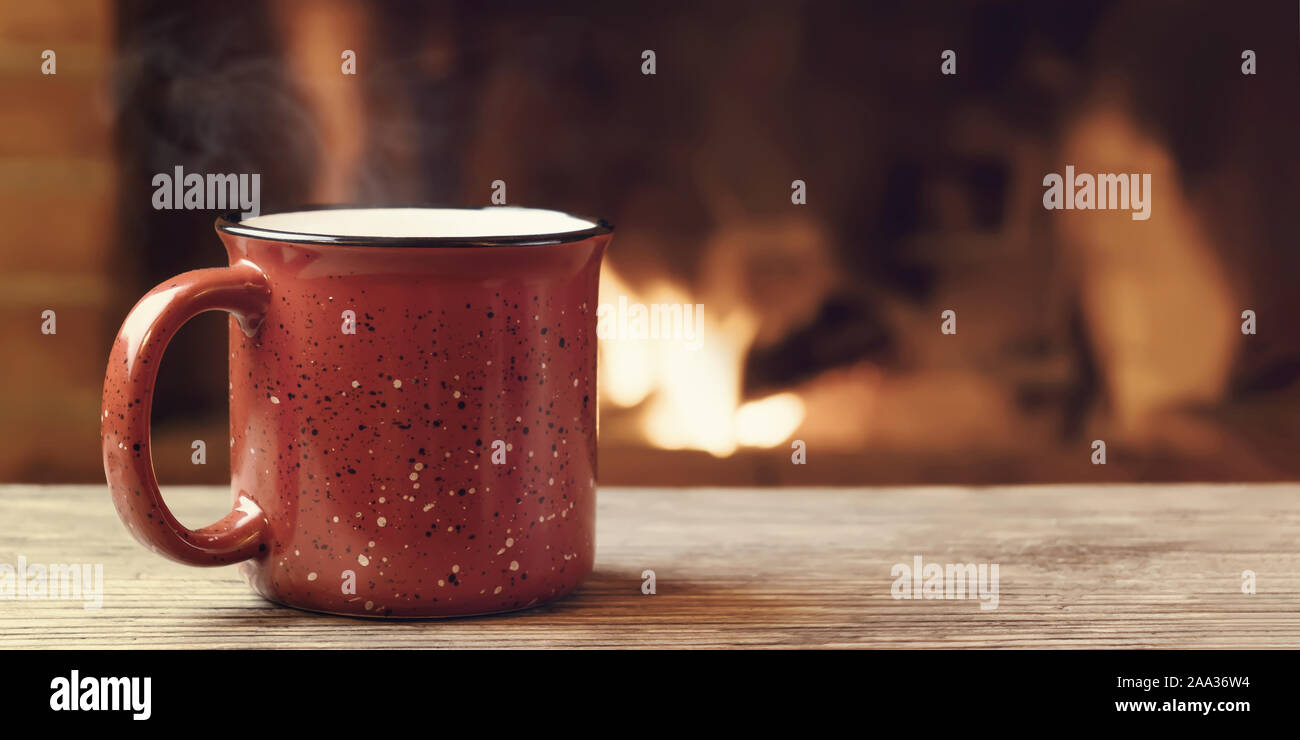 Rot Tasse mit heißem Tee vor einem brennenden Kamin, Komfort, Winterurlaub und Wärme des Herdes Konzept. Stockfoto