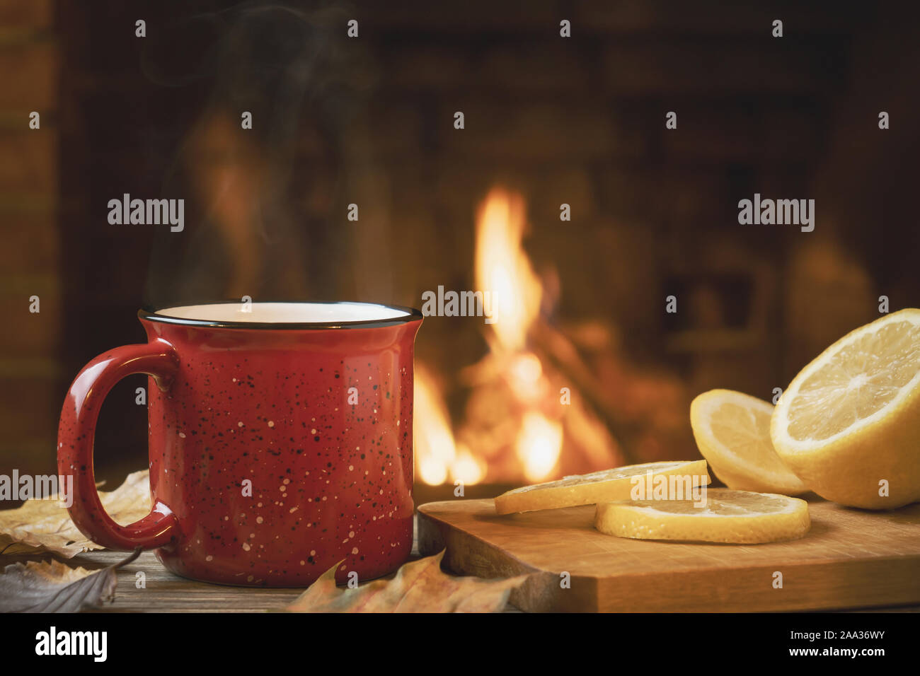 Rot Tasse mit heißem Tee mit Zitrone vor einem brennenden Kamin, Komfort und Wärme des Herdes Konzept. Stockfoto