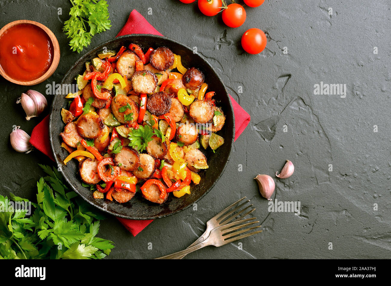 Scheiben von gebratenem Gemüse mit Würstchen und Gewürzen in einer Pfanne über schwarzen Stein Hintergrund mit kopieren. Ansicht von oben, flach Stockfoto