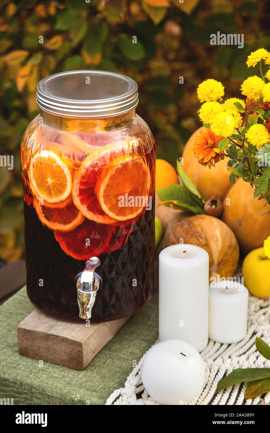 Glühwein in einem Glaszylinder auf einem Tisch im Garten für ein festliches Abendessen mit der Familie neben Kerzen, Kürbisse und Blumen. Einrichtung und Tabelle einstellen. Stockfoto