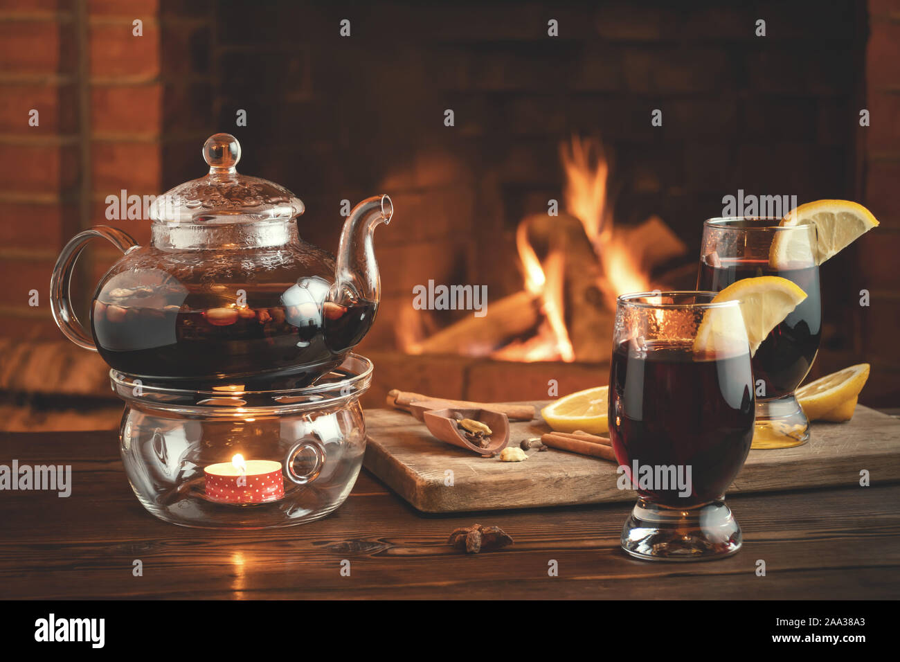 Zwei Gläser von Glühwein und Teekanne auf einem holztisch vor einem brennenden Kamin. Stockfoto