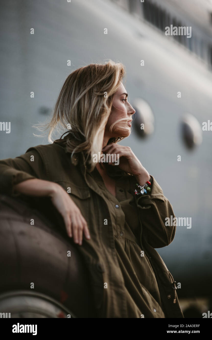 Schöne blonde Frau im grünen Mantel steht in der Nähe der alten Flugzeug Rad. Stockfoto