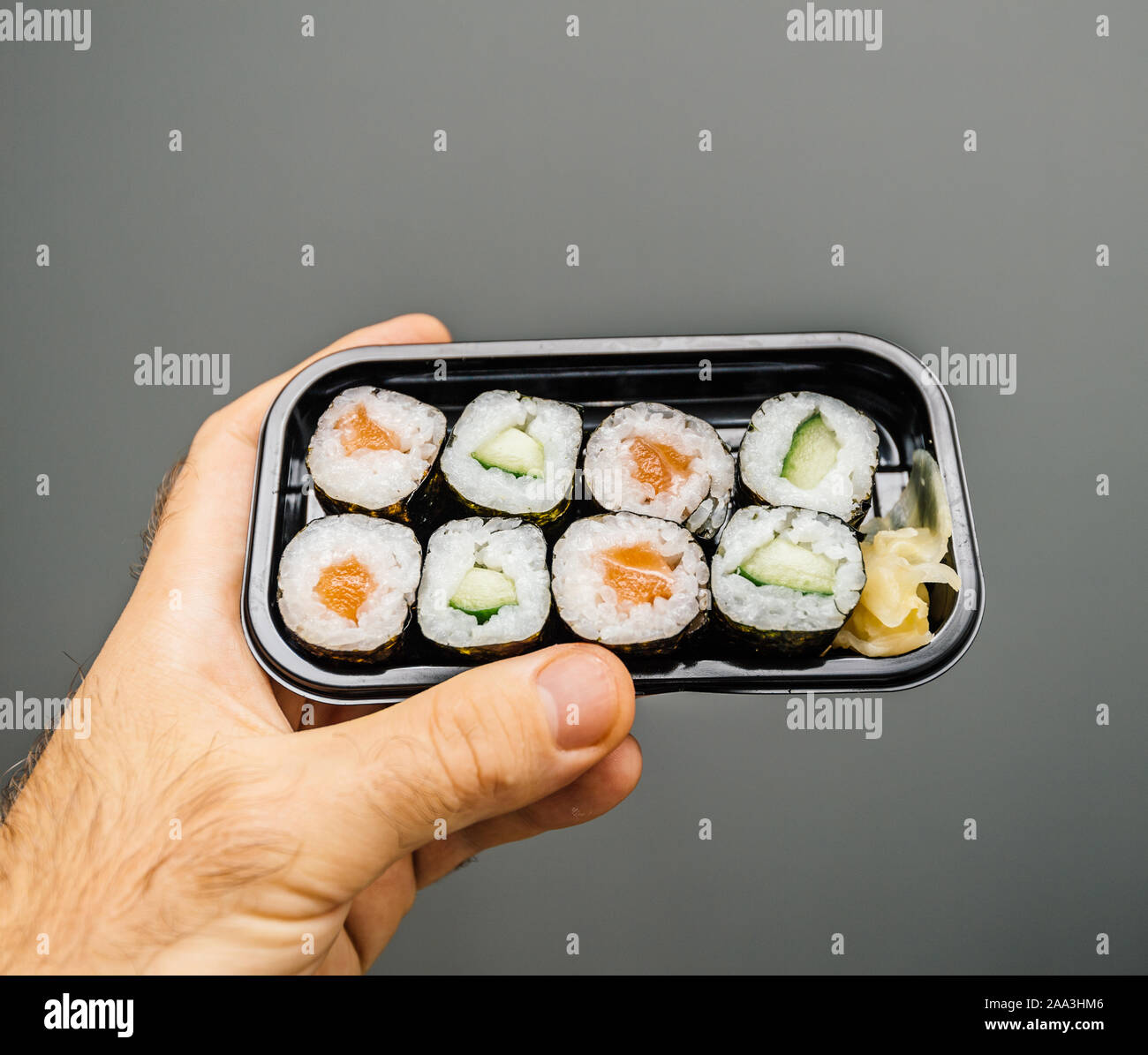 Mann Hand köstliches Sushi maki schwarzen Kunststoffbox mit leckeren Bio Zutaten auf grauem Hintergrund Stockfoto