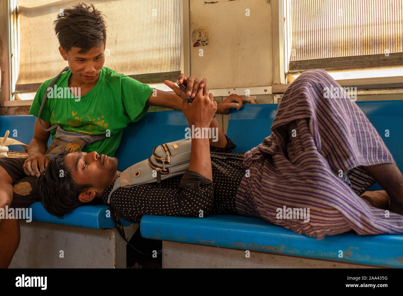 Zwei Jungen burmesischen Anbieter machen Sie eine Pause und einem Handy prüfen, während auf einem lokalen Zug auf dem Rundweg um Yangon, Myanmar (Birma) Stockfoto