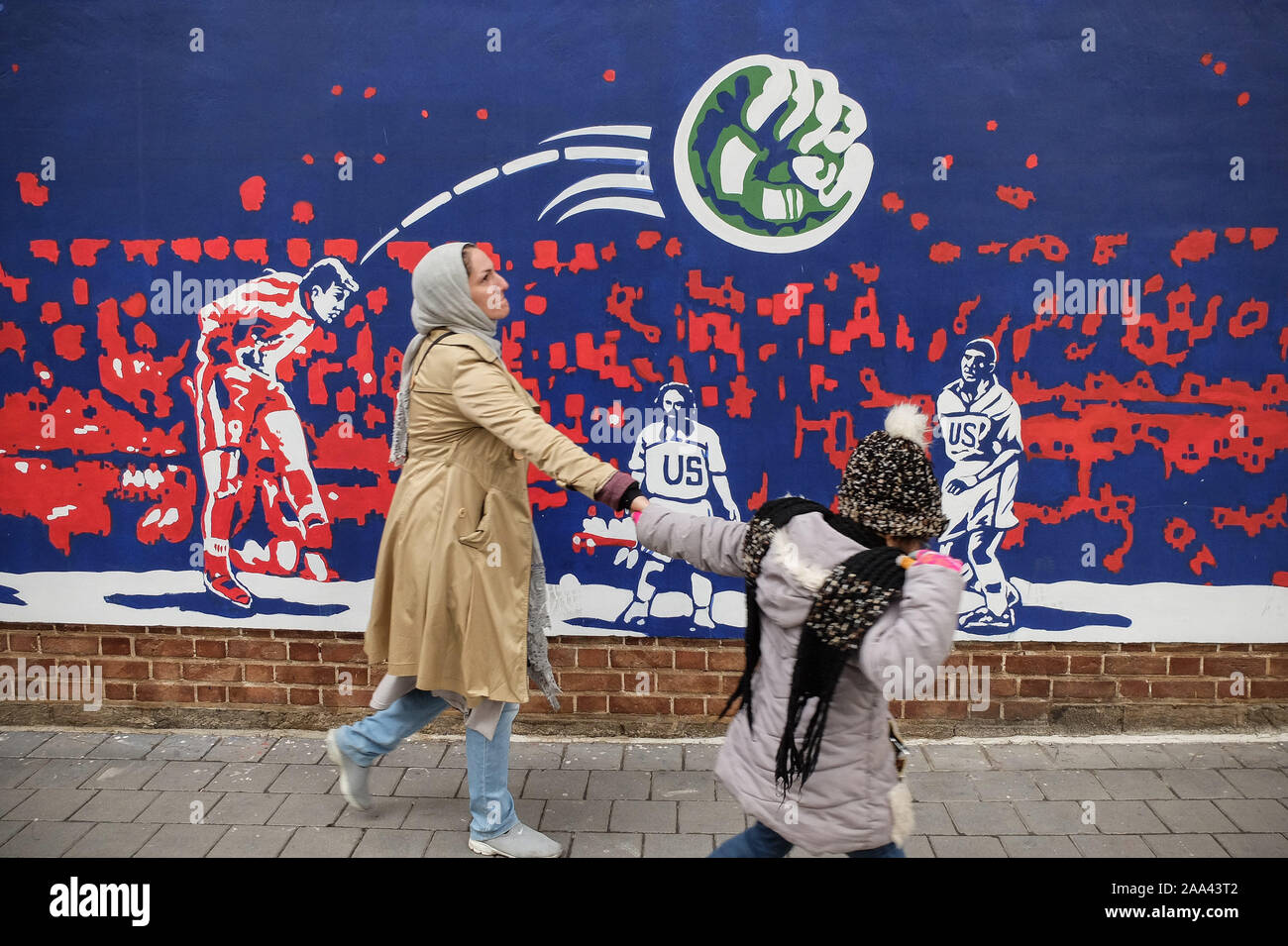 Teheran, Iran. Nov, 2019 19. Eine Frau und ihr Kind vorbei eine Wandmalerei an der Wand entlang der ehemaligen US-Botschaft in Teheran, Iran. Drei Sicherheit Personal wurden von "randalierer" im Iran, die jüngsten Todesfälle in den Protesten, dass keine Anzeichen für eine nachlassende Dienstag Trotz einer Welle von Verhaftungen und Internet shutdown zeigten getötet. Die Todesfälle zu mindestens fünf die Zahl der Menschen, die bestätigt, dass in der bundesweiten Demonstrationen am Freitag gegen einen Schock Entscheidung benzin Preiserhöhungen zu verhängen ausbrach, getötet worden sein. Die Situation auf den Straßen bleibt unklar, vor allem wegen der Regierung-impos Stockfoto