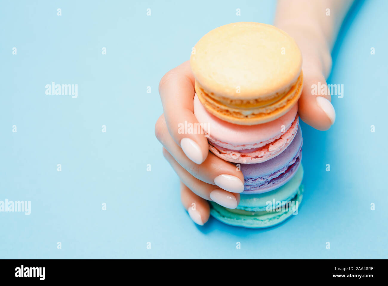 Schönheit hand Mädchen mit trendigen Maniküre unter Farbe makronen auf blauem Hintergrund. Stockfoto