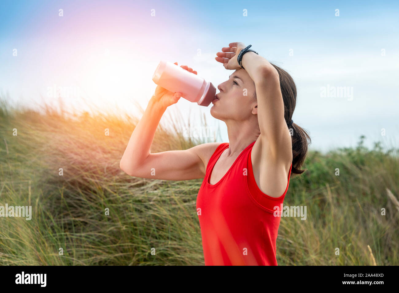 Frau trinkt aus einer Wasserflasche während draußen in der Sonne exercicing Stockfoto