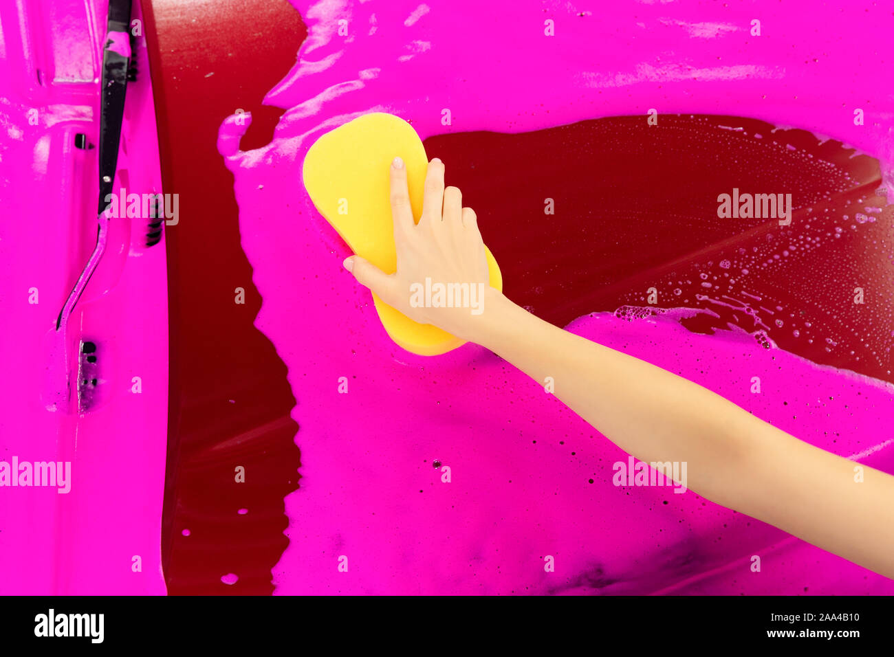 Hand halten, gelben Schwamm über Auto waschen rosa Schaum Hintergrund. Ansicht von oben. Stockfoto