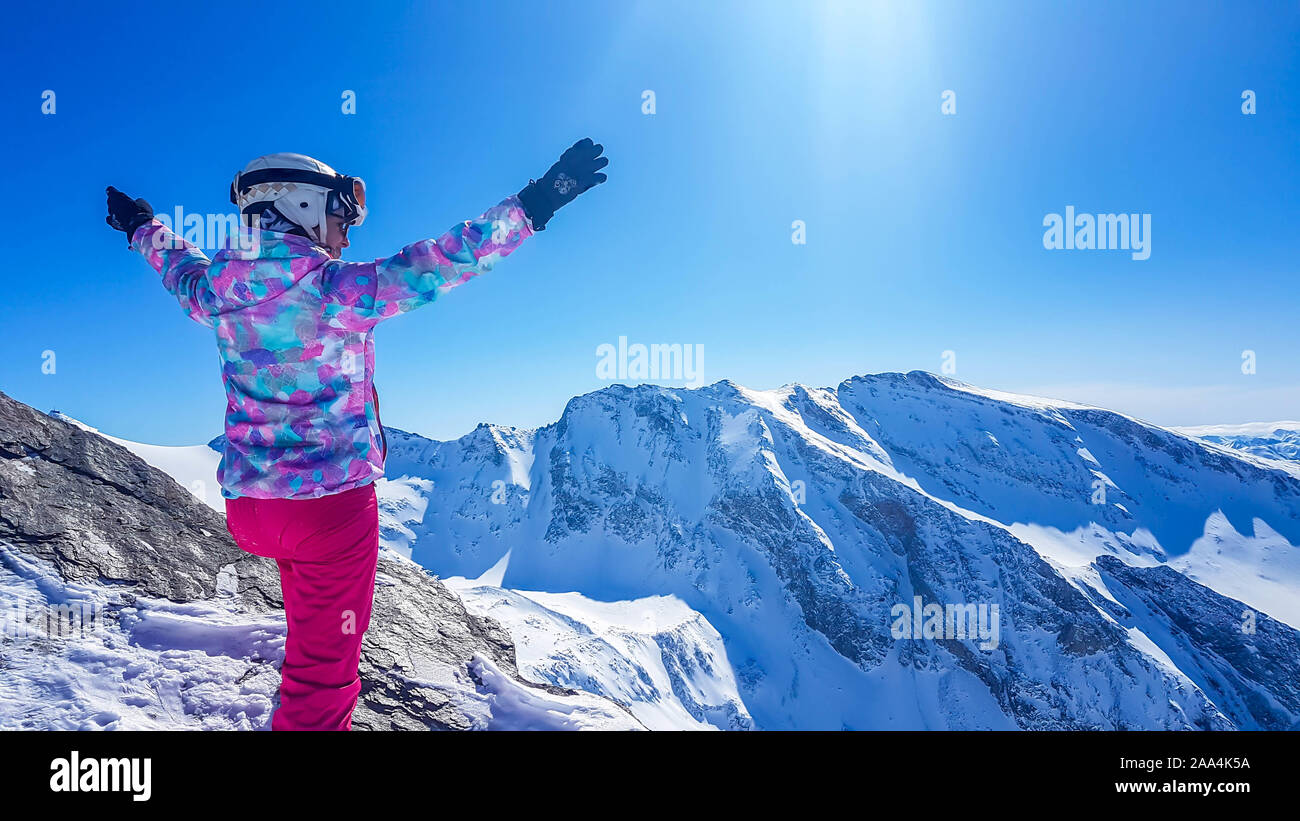 Snowboarder Mädchen mit erhobenen Händen in Heiligenblut, Österreich. Bedeckt mit Wolken. Sie trägt bunte Jacke, Sonnenbrille und Helm. Smiley Stockfoto
