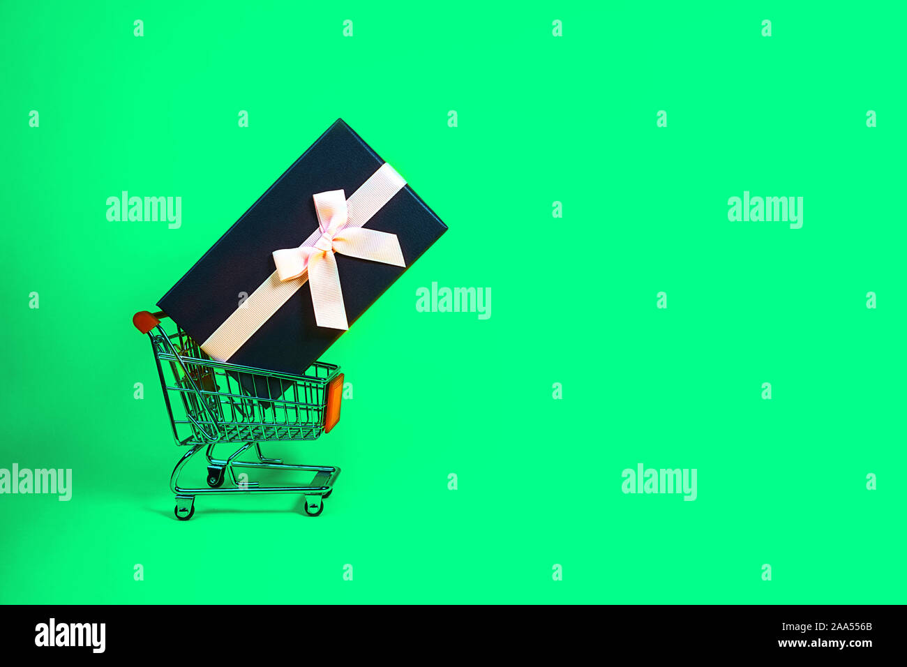 Urlaub Geschenk, Schwarz Grün Freitag Konzept mit Geschenkbox und rosa Schleife in einem Metall Einkaufswagen, Korb auf grüne Farbe Hintergrund. Shopping. Outfit. Flach, Ansicht von oben, Platz für Text. Stockfoto