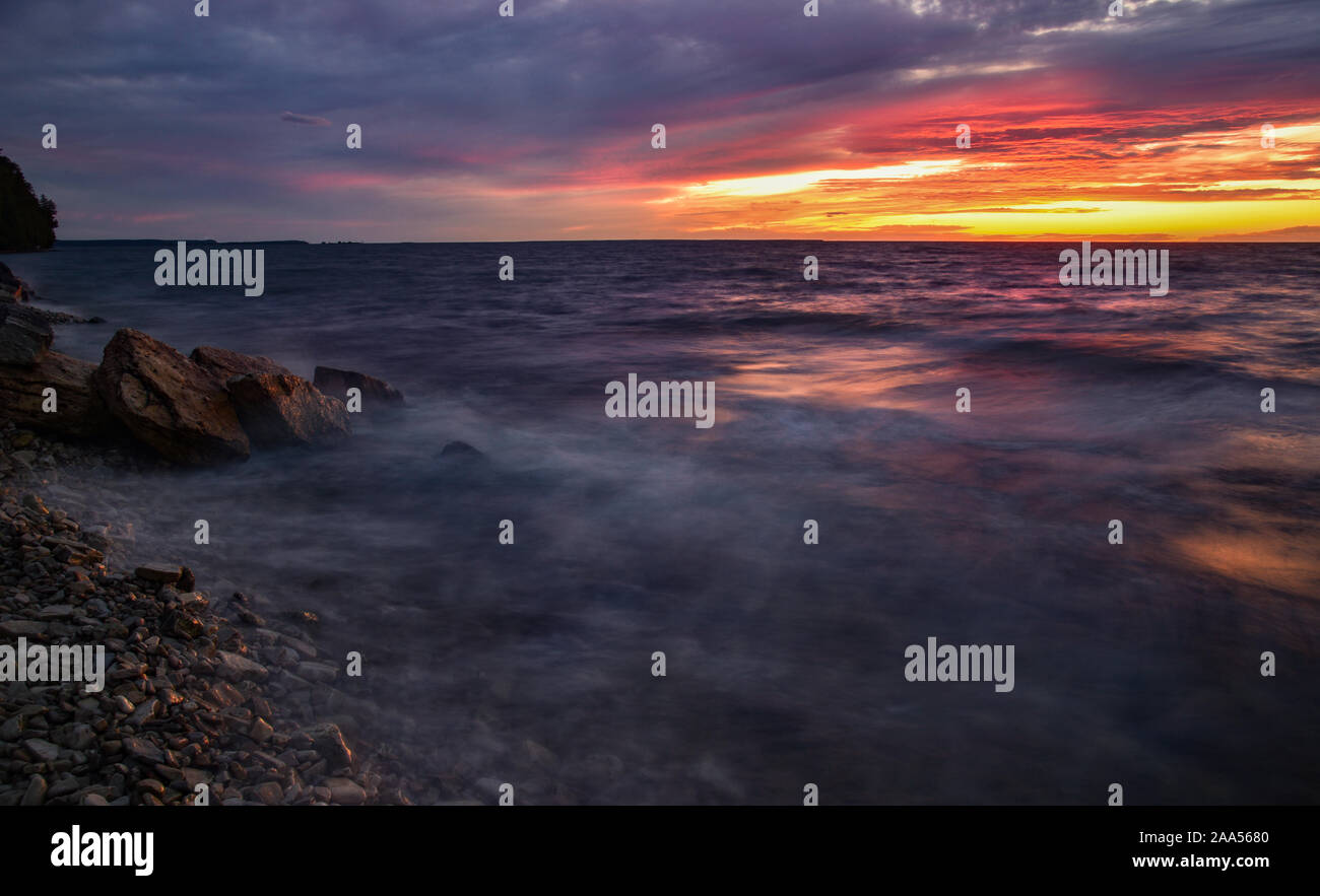 Schönen Sonnenuntergang über Green Bay mit wirbelnden Wasser in Bewegung, Streifen über die Felsen und Spritzwasser entlang der Küste in der Nähe von Ellison Bay, Wisconsin, USA Stockfoto