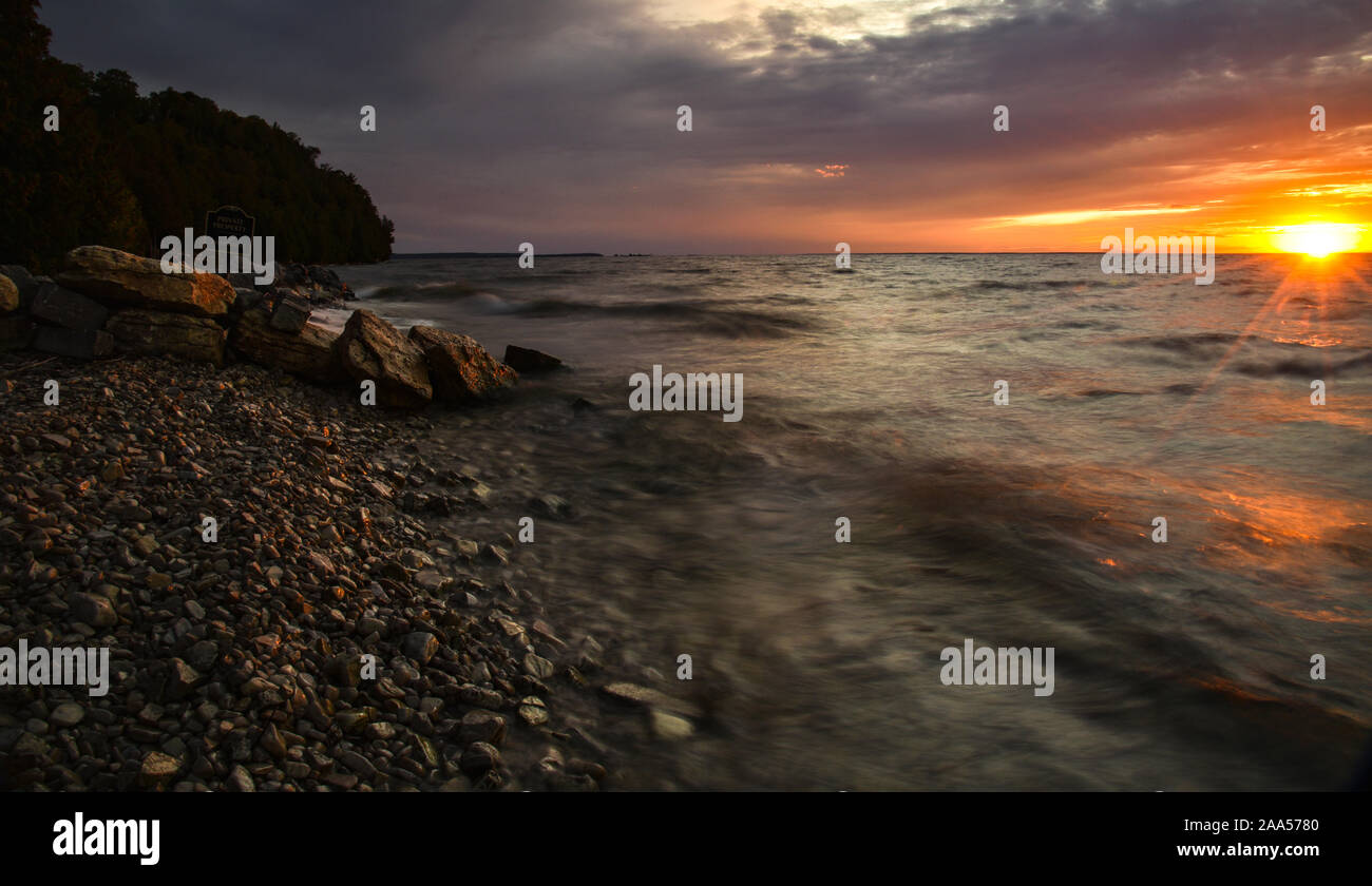 Schönen Sonnenuntergang über Green Bay mit wirbelnden Wasser in Bewegung, Streifen über die Felsen und Spritzwasser entlang der Küste in der Nähe von Ellison Bay, Wisconsin, USA Stockfoto