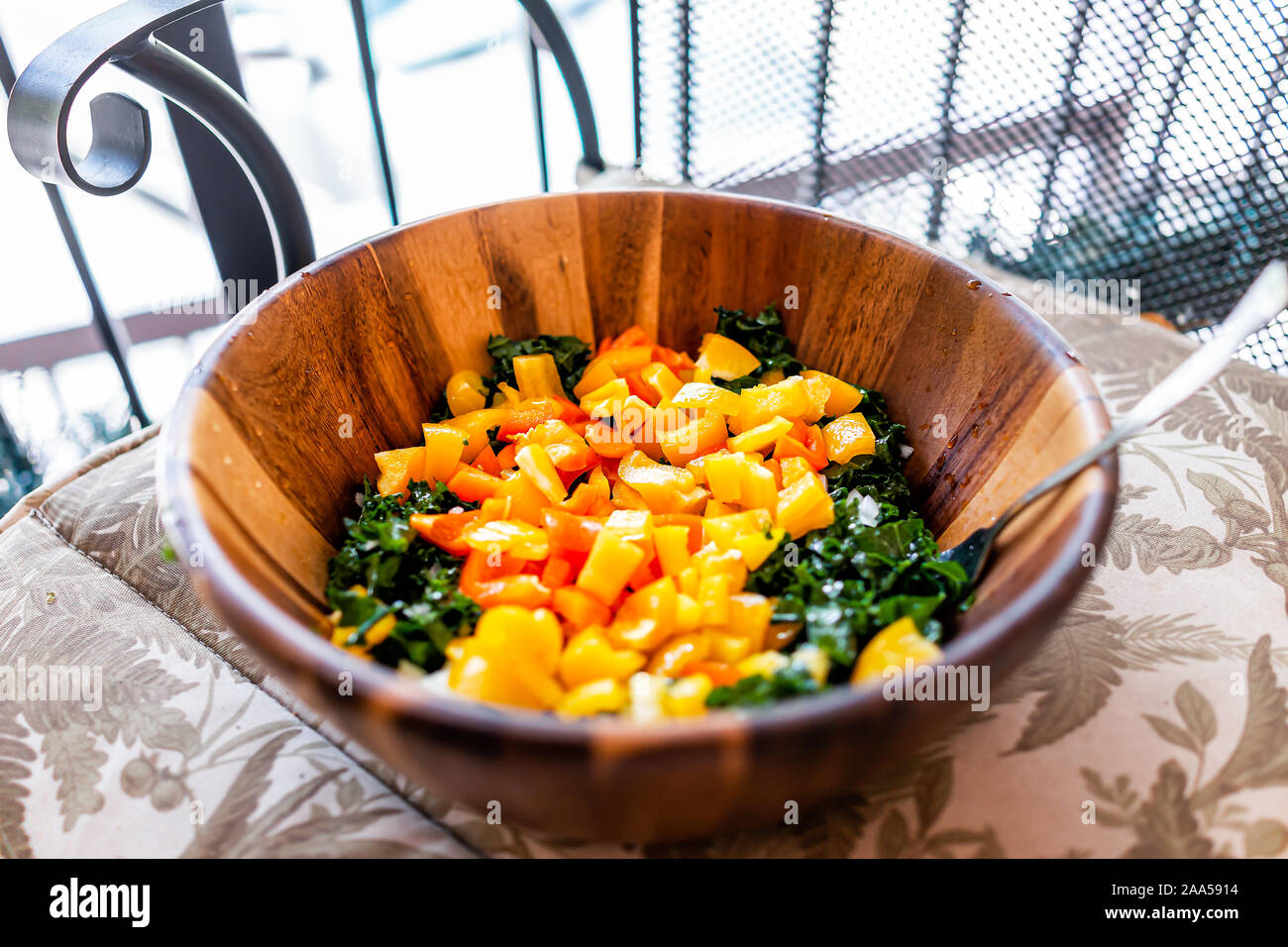 Nahaufnahme eines großen hölzernen Salatschüssel mit gehackten Grünkohl und  orange-gelbe Paprika als vegan Mittag- oder Abendessen auf dem Balkon Stuhl  Stockfotografie - Alamy