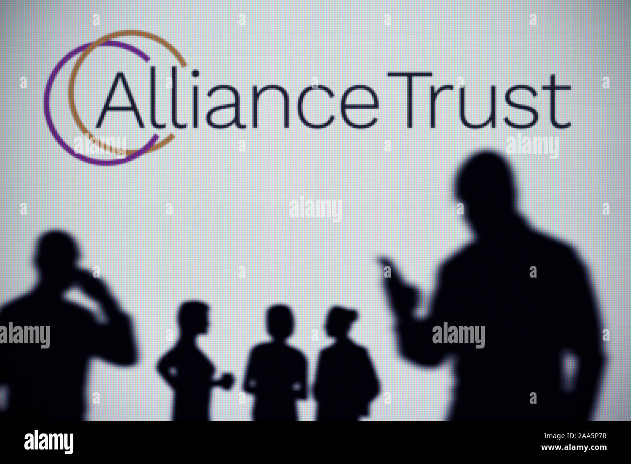 Die Alliance Trust Logo ist auf einen LED-Bildschirm im Hintergrund, während eine Silhouette Person ein Smartphone verwendet (nur redaktionelle Nutzung) Stockfoto